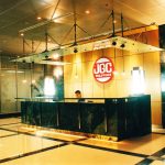 Modern corporate reception desk with black paneling, cream countertop, and red JGC logo